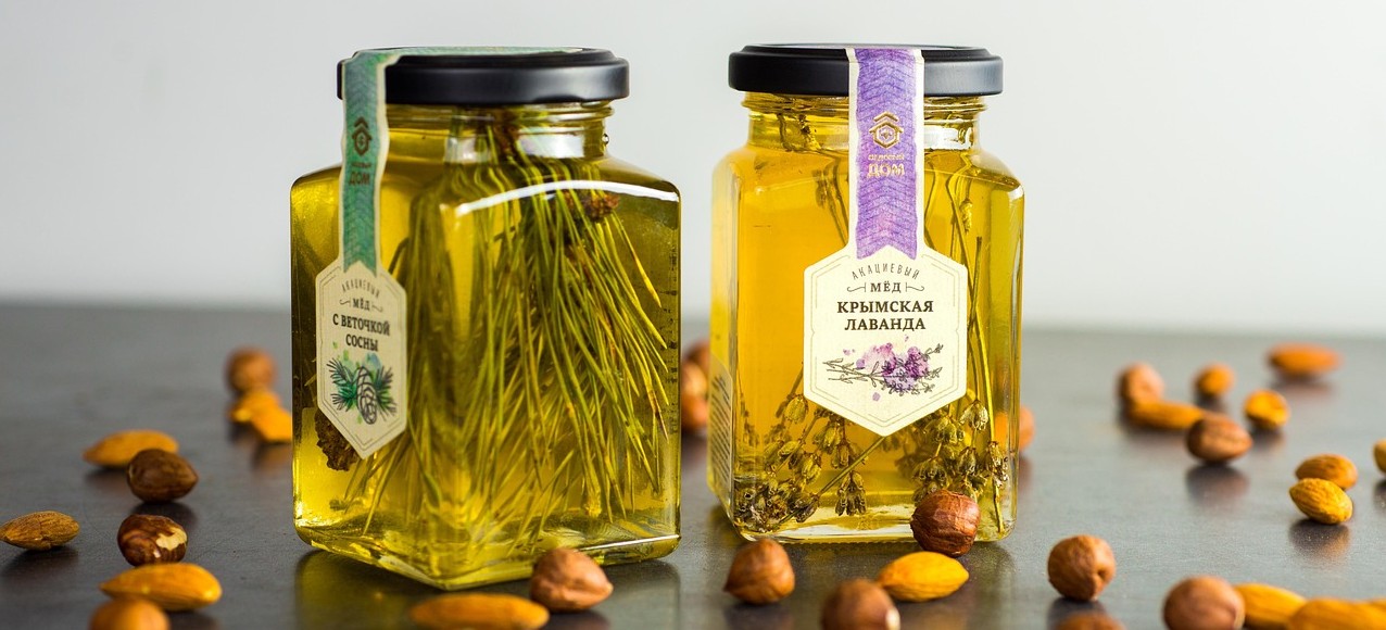Two jars of honey on display with nuts scattered around them