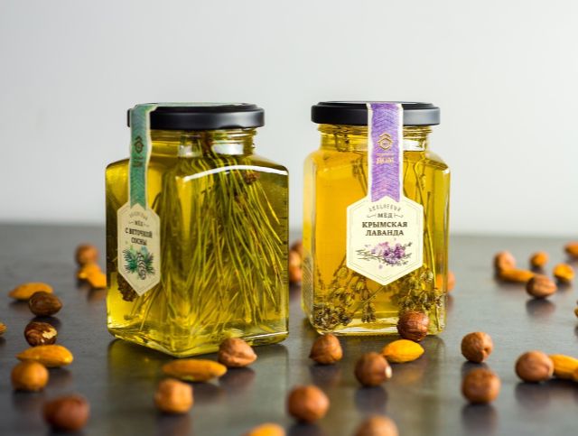 Two jars of honey on display with nuts scattered around them